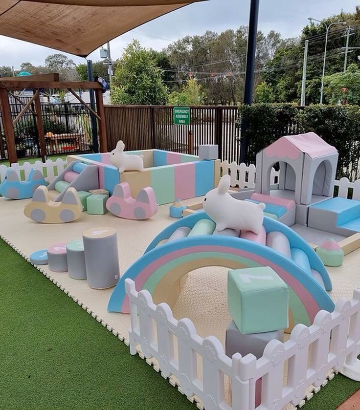 Outdoor pastel soft play rental setup on artificial grass with white picket fence and rainbow arch